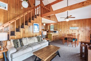 A wooden interior with a sofa, a dining table, and a kitchen area. - Owl's Nest -- Vacay Your Way with Flexible Arrival and Stay Dates (Kill Devil Hills)