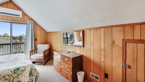 Ein Schlafzimmer mit einem Bett, einem Sessel, einem Schminktisch, einem Spiegel und einer Tür.