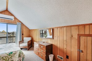A bedroom with a bed, a chair, a dresser, a mirror, and a door. - Owl's Nest -- Vacay Your Way with Flexible Arrival and Stay Dates (Kill Devil Hills)