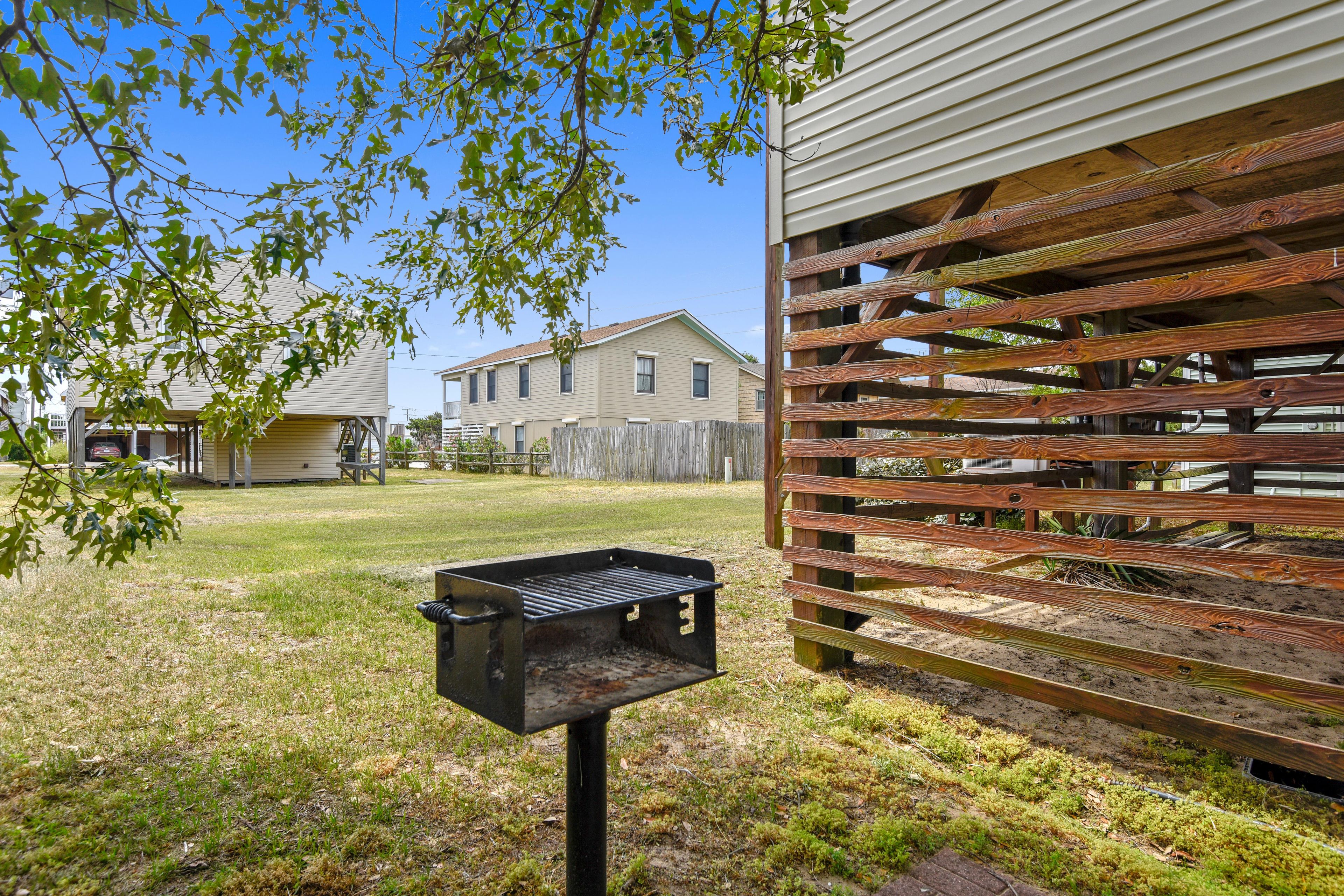 Un patio trasero con una parrilla, cerca de madera y casas al fondo.