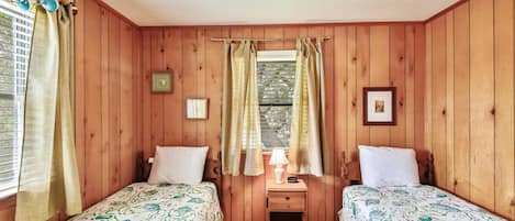A room with two beds, a nightstand, a window with curtains, and a wall clock.