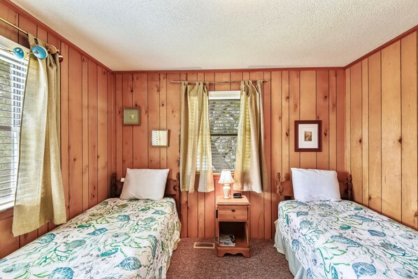 A room with two beds, a nightstand, a window with curtains, and a wall clock.