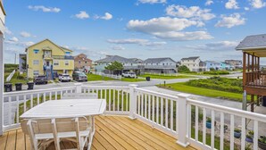 A wooden deck with a table and chairs, overlooking a residential street with houses and parked cars. - Gone to Carolina -- Recently Remodeled Home with Pool, Hot Tub, & Putting Green (Kitty Hawk)