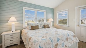 A bedroom with a bed, two bedside tables, a nightstand, and a door. - Gone to Carolina -- Recently Remodeled Home with Pool, Hot Tub, & Putting Green (Kitty Hawk)