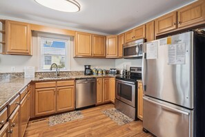A modern kitchen with wooden cabinets, stainless steel appliances, and a granite countertop. - Gone to Carolina -- Recently Remodeled Home with Pool, Hot Tub, & Putting Green (Kitty Hawk)