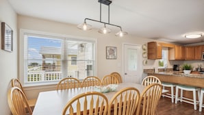 A dining area with a table and chairs, a kitchen with wooden cabinets, and a window with blinds.