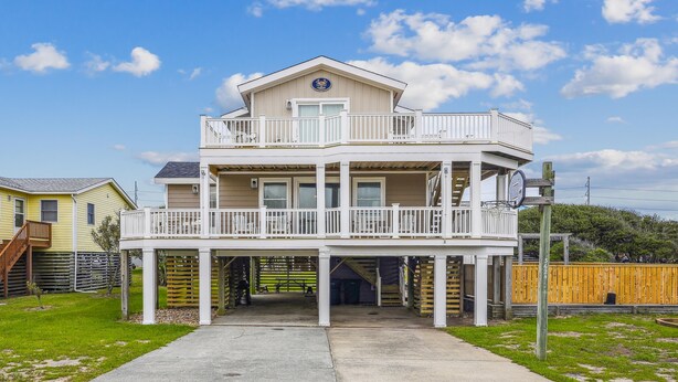 A two-story beachfront house with a balcony, a covered entryway, and a visible garage door. - Gone to Carolina -- Recently Remodeled Home with Pool, Hot Tub, & Putting Green (Kitty Hawk)