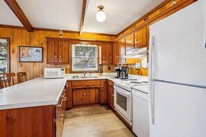 A kitchen with wooden cabinets, a white countertop, a microwave, a sink, a stove, and a refrigerator.