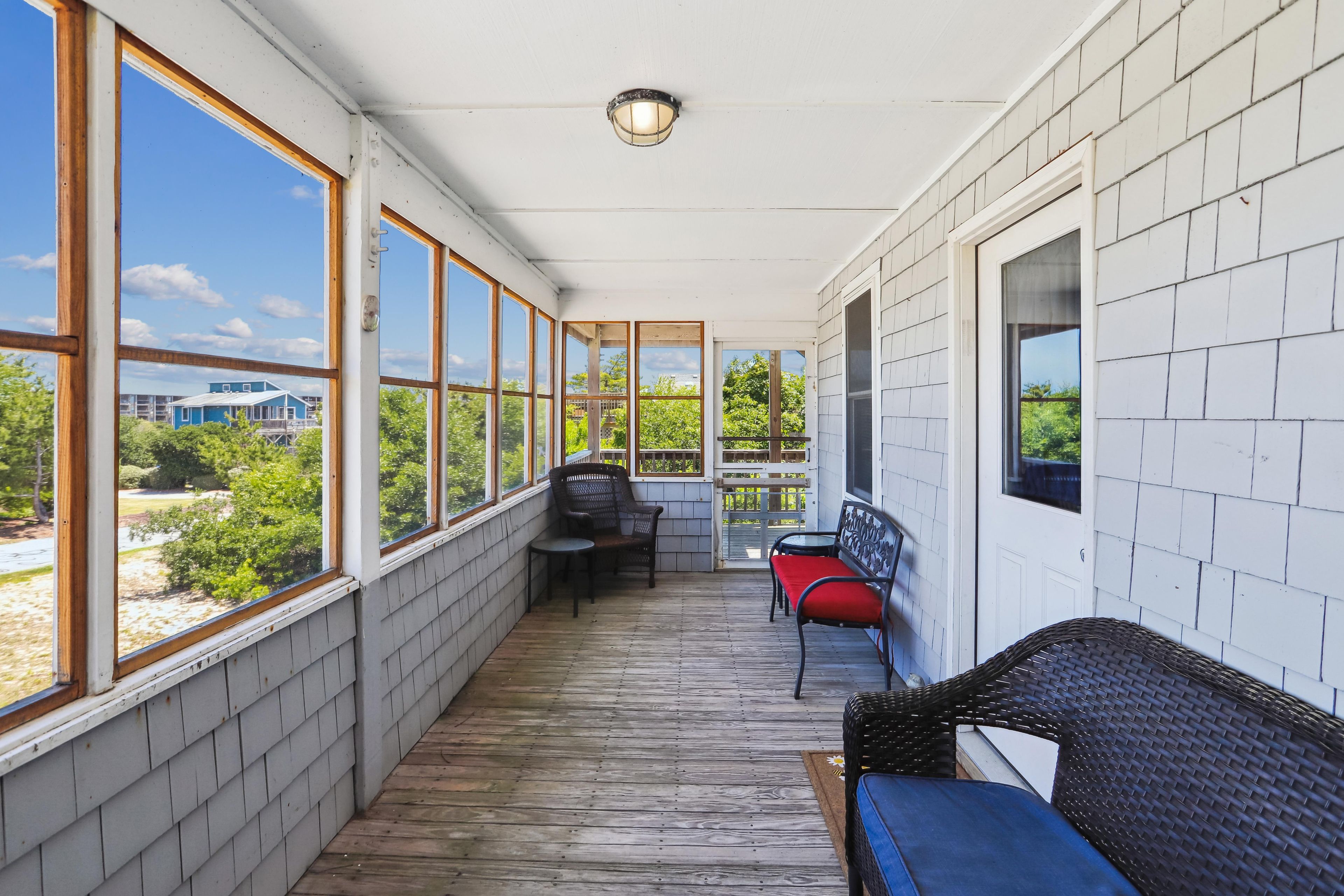 A covered porch with a wooden floor, a table, two chairs, and a bench.