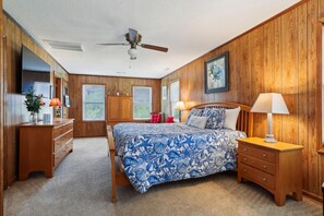A bedroom with a bed, wooden walls, a ceiling fan, and a window.
