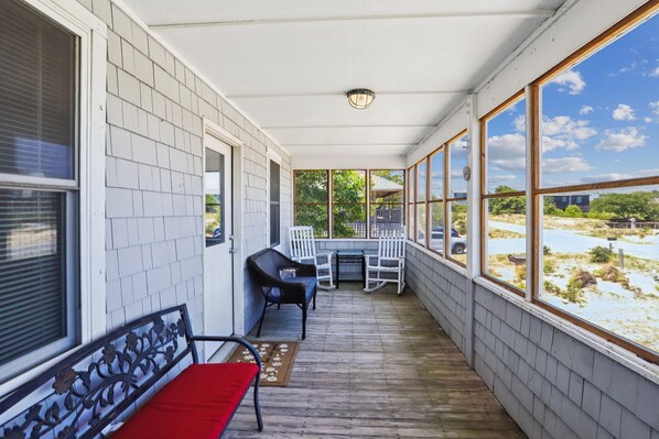 A covered porch with a table and chairs, a bench, and a view of the landscape.