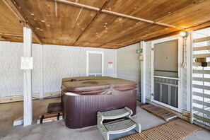 Un jacuzzi en un espacio exterior cubierto, con techo de madera, una puerta y un banco.