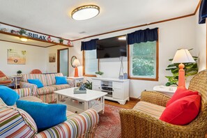 A cozy living room with striped sofas, a flat-screen TV, and a small table. - Doris's Day-- 4BR Oceanside home in Duck with Private Hot Tub (Duck)