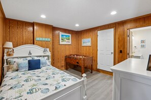 A bedroom with a bed, a wooden wall, a door, and a foosball table.