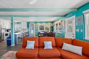 A kitchen with white cabinets, a dining area with a table and chairs, and a living room with an orange sofa and decorative pillows. - Surf N Sound -- Pet Friendly 4BR with Ocean and Sound Views in Duck (Duck)