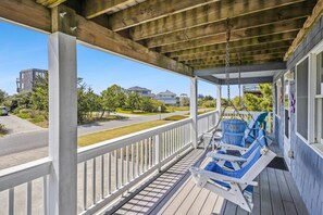 A covered porch with a swing chair, a white railing, and a view of a residential street.