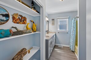 Un couloir étroit menant à une salle de bain dotée d’une fenêtre, d’un rideau de douche orné d’un motif de tortue de mer et d’un panneau mural décoré d’un motif de vague.