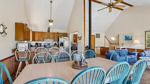 A spacious kitchen with wooden cabinets, a dining area with blue chairs, and a ceiling fan. - The Tree House --Flexible Arrival and Stay Dates Year Round (Duck)