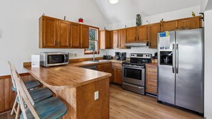 A kitchen with wooden cabinets, a stainless steel refrigerator, a microwave, an oven, and a coffee maker. - The Tree House --Flexible Arrival and Stay Dates Year Round (Duck)