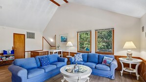 A living room with a blue sectional sofa, a white coffee table, and two windows with views of greenery. - The Tree House --Flexible Arrival and Stay Dates Year Round (Duck)