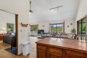 A spacious kitchen with a wooden island, a dining area with chairs, a sofa, and a TV. There is a balcony with a view of greenery. - The Tree House --Flexible Arrival and Stay Dates Year Round (Duck)