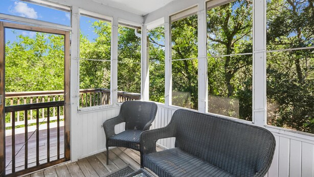 A covered porch with wicker furniture, a glass table, and a view of trees. - The Tree House --Flexible Arrival and Stay Dates Year Round (Duck)
