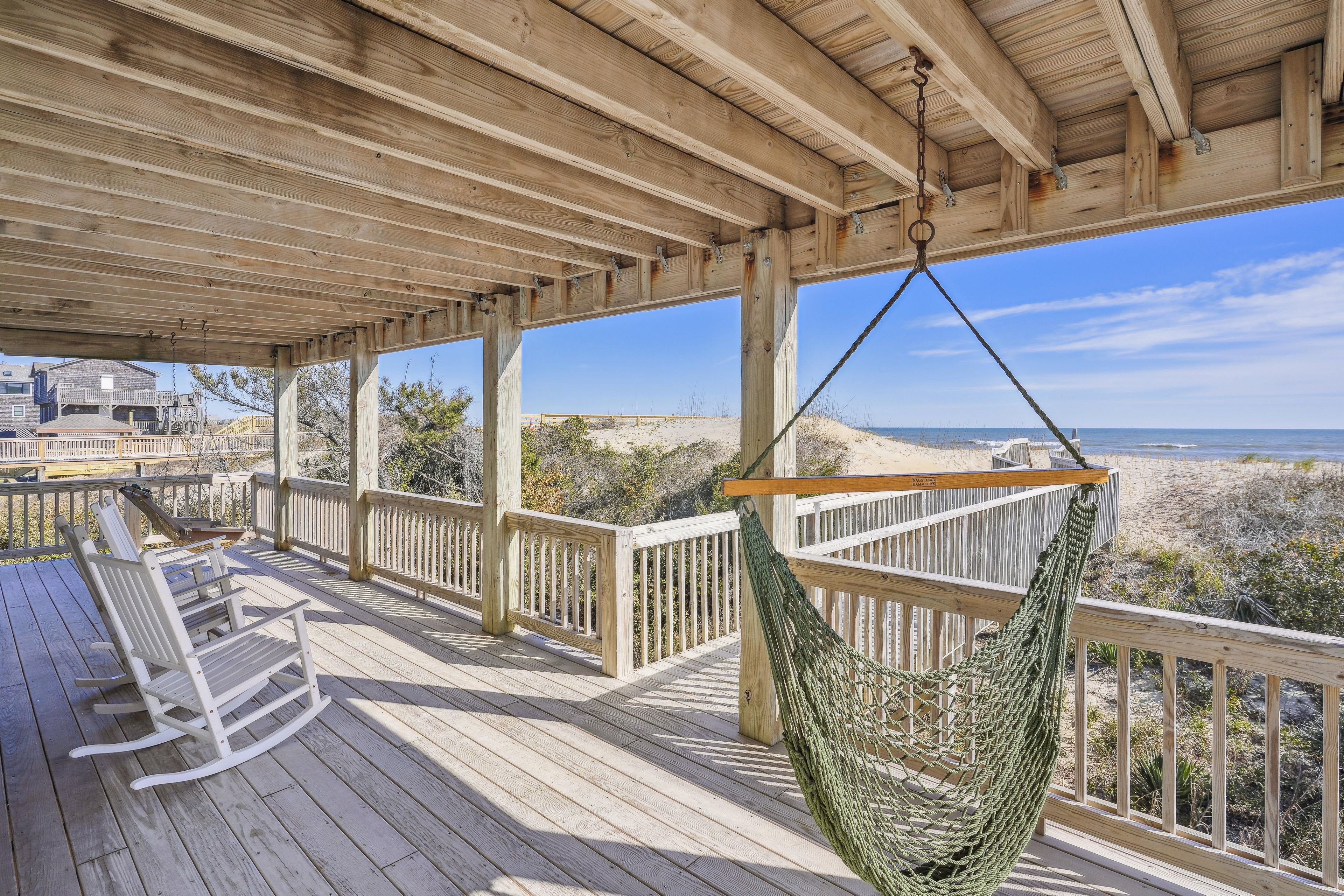 Une terrasse en bois avec un hamac, des rampes en bois et une vue sur la plage.