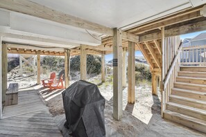 Un espace extérieur abrité doté d’une terrasse en bois, d’un coin salon couvert et d’un escalier menant à un niveau supérieur.