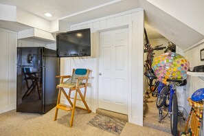 Een knus woongedeelte met een koelkast, een aan de muur bevestigde televisie, een houten stoel en een fiets met een kleurrijke mand.