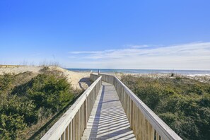 Une promenade en bois qui mène à une plage bordée de dunes et dotée d’une végétation clairsemée.