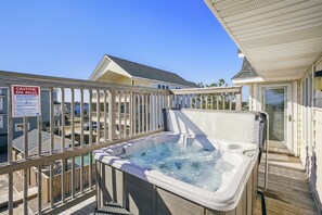 Een hottub op een houten terras met een veiligheidsteken, omringd door een houten hek en een gebouw op de achtergrond.
