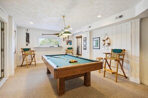 A pool table in a room with white walls, a ceiling fan, and a window.