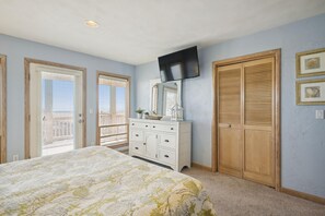 Une chambre à coucher comprenant un lit, une commode, un téléviseur et deux portes.