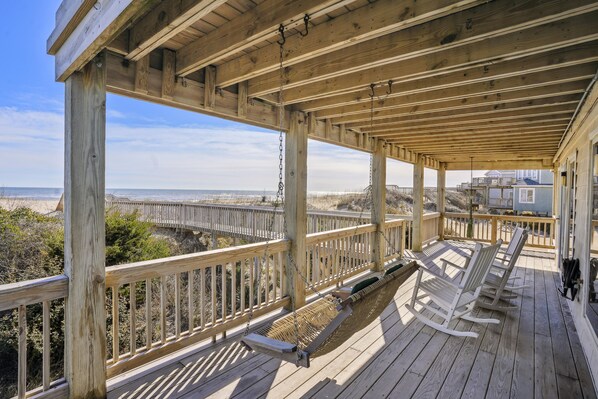 A wooden deck with a view of the beach and a bridge.
