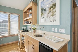 A kitchen with a wooden countertop, a sink, and a window with blinds. There is a shelf with books and a plant.