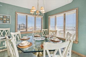 A dining area with a glass table, white chairs, and a view through large windows.