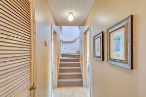 A hallway with a carpeted staircase, wooden blinds, and framed pictures on the walls. - Sea Duck Sun -- Dog Friendly 5BR in Downtown Duck (Duck)