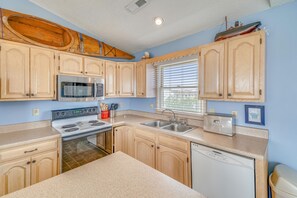 A kitchen with wooden cabinets, a microwave, a stove, a sink, and a window with blinds. - Sea Duck Sun -- Dog Friendly 5BR in Downtown Duck (Duck)