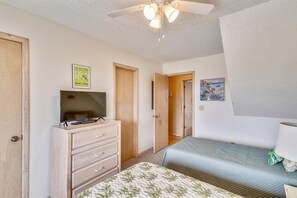 A bedroom with a bed, a TV on a dresser, a ceiling fan, and a door leading to another room. - Sea Duck Sun -- Dog Friendly 5BR in Downtown Duck (Duck)