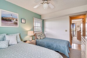A bedroom with two beds, a ceiling fan, a window with blinds, a nightstand with a lamp, and a framed picture on the wall. - Sea Duck Sun -- Dog Friendly 5BR in Downtown Duck (Duck)