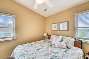 A bedroom with a bed, two wall-mounted pictures, a ceiling fan, and windows with blinds. - Sea Duck Sun -- Dog Friendly 5BR in Downtown Duck (Duck)