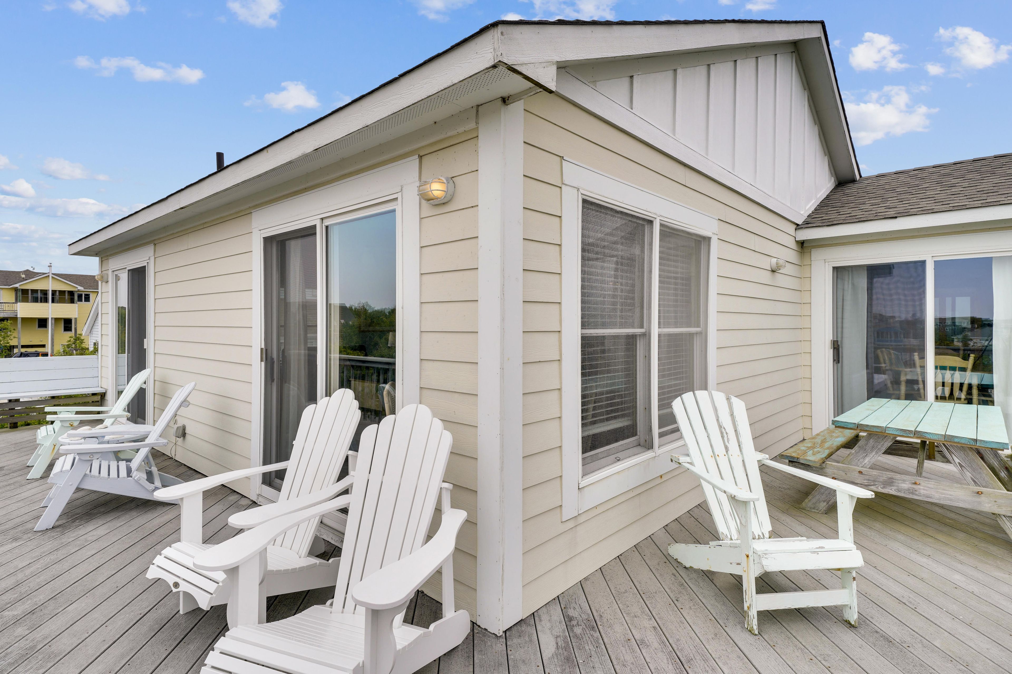 A house with a deck featuring white Adirondack chairs and a table.