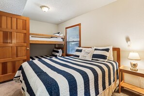 Une chambre avec un lit superposé, une table de chevet avec une lampe et une fenêtre avec des stores.