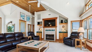 Ein großzügiges Wohnzimmer mit Kamin, Ledersofas und Deckenventilator.
