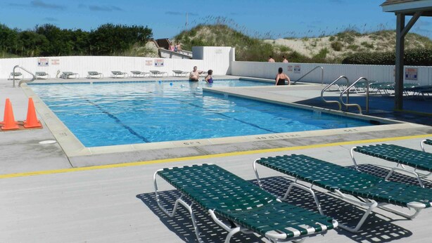Ein Schwimmbecken mit mehreren Bahnen, Liegestühlen und einem überdachten Bereich.