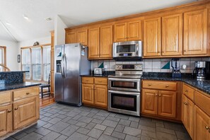 A modern kitchen with wooden cabinets, stainless steel appliances, and a granite countertop. - Ocean Paradise -- Spacious 7BR Oceanfront with Pool, Hot Tub and More! (Corolla)