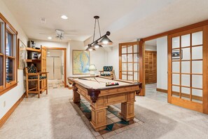 Une table de billard dans une pièce dotée d’un plancher en bois, d’un ventilateur de plafond et d’une carte accrochée au mur.