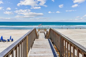 A wooden boardwalk leading to a beach with a flag. - Ocean Paradise -- Spacious 7BR Oceanfront with Pool, Hot Tub and More! (Corolla)
