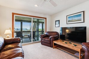 A living room with a brown leather sofa, a wooden coffee table, a television, and a fireplace. - Ocean Paradise -- Spacious 7BR Oceanfront with Pool, Hot Tub and More! (Corolla)