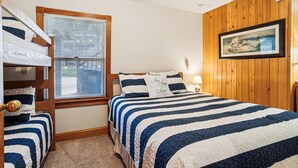 Ein Schlafzimmer mit Etagenbetten, einem großen Fenster mit Jalousien, einem Bett mit gestreifter Bettdecke, einem Wandbild und einer Holztür.